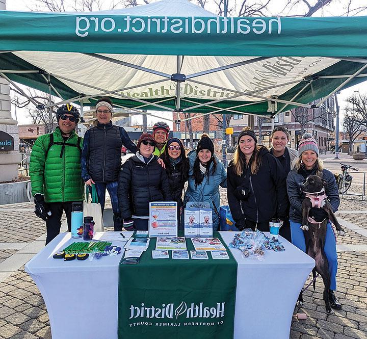 Foto de grupo del personal del Distrito de Salud detrás de la estación de trabajo en bicicleta de invierno del Distrito de Salud en Oak Street Plaza en Fort Collins Colorado